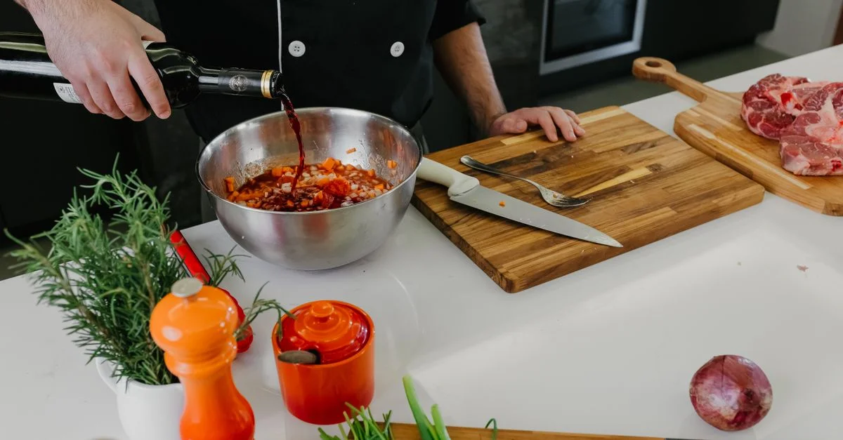 Chef versant du vin rouge dans un bol avec des herbes et des épices pour la préparation de la marinade.