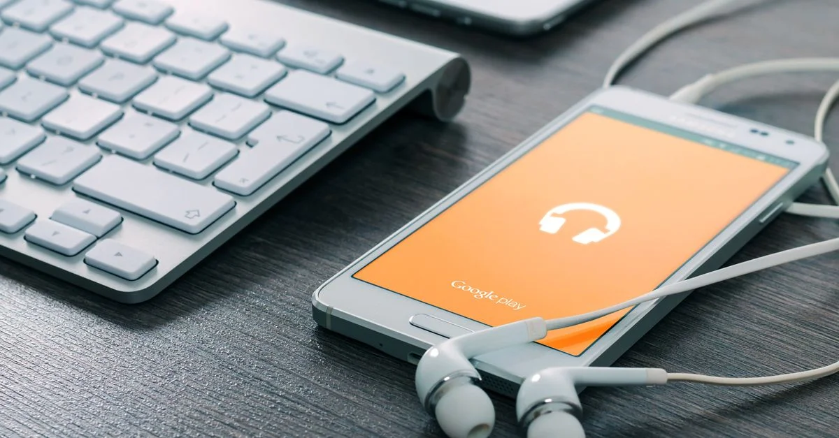 Un smartphone avec des écouteurs connectés à côté d'un clavier sur un bureau en bois, mettant en avant la technologie moderne.