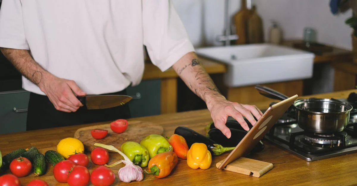 Homme adulte préparant des légumes avec un couteau et une tablette dans une cuisine moderne.