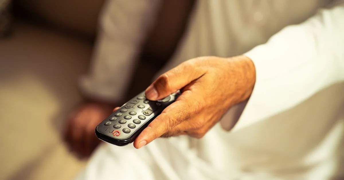 Gros plan sur la main d'un adulte tenant une télécommande, se détendant à l'intérieur.