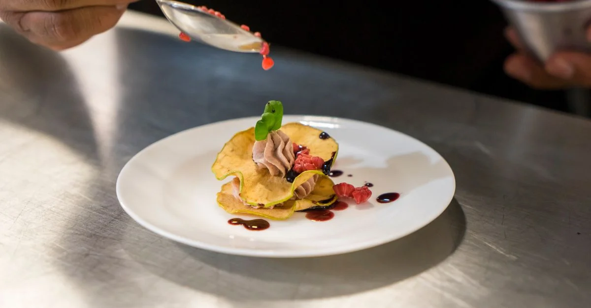 Gros plan d'un chef dressant un dessert élégant avec une sauce aux baies sur une assiette blanche.