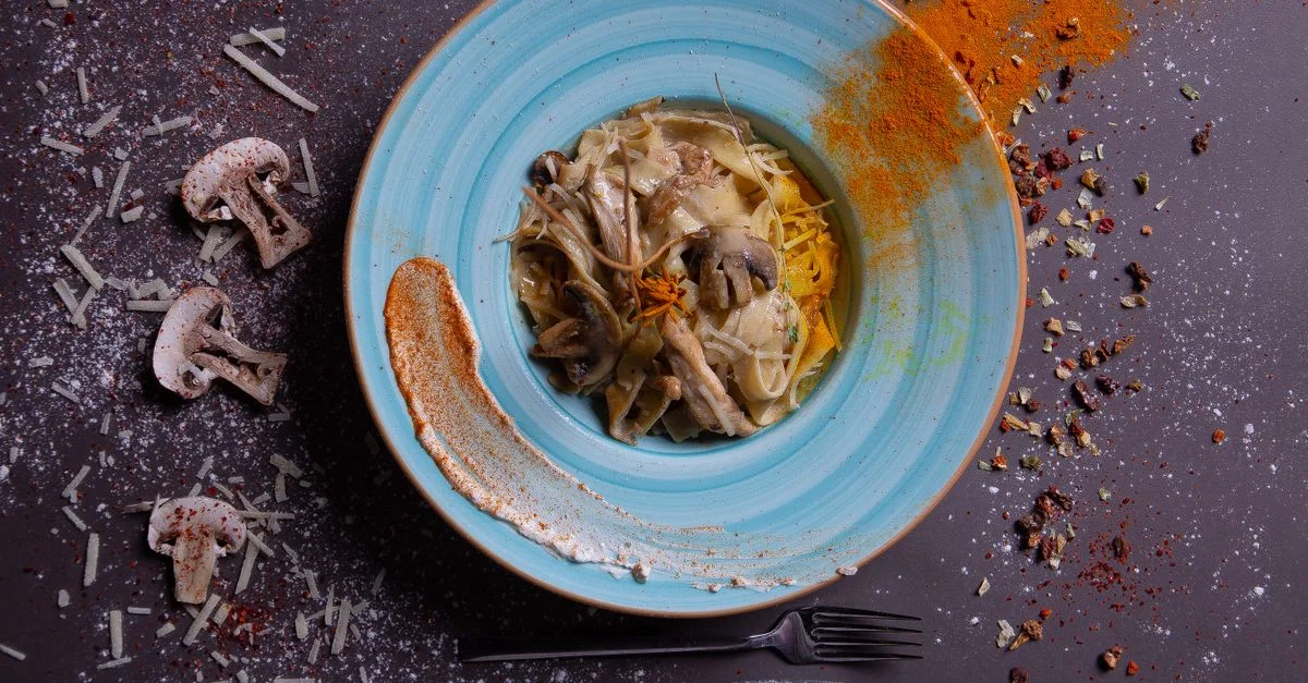Un délicieux plat de pâtes aux champignons et aux épices, artistiquement présenté sur une assiette turquoise.